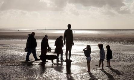 A family with children around one of the Antony Gormley statues ( Another Place ) Crosby Beach, Liverpool, Merseyside, UK